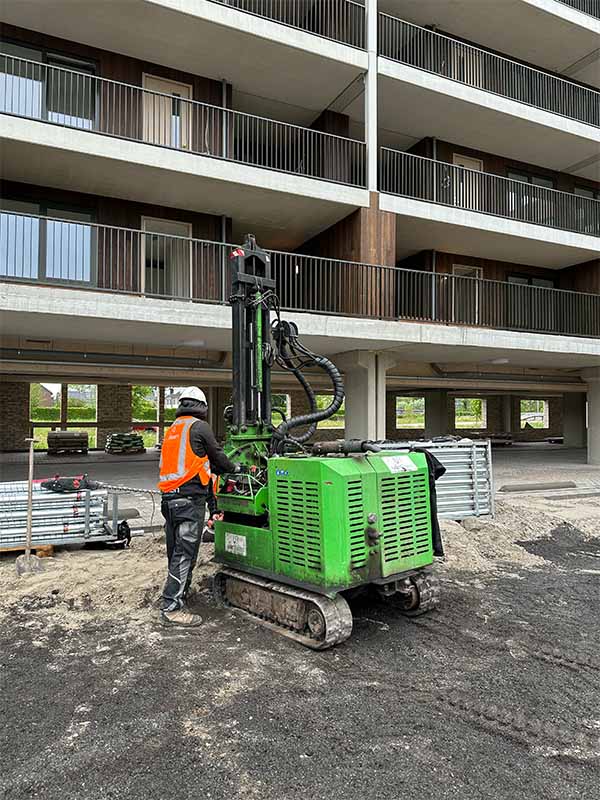 Van Aken monteur bedient groene schroefpaal machine onder moderne appartementencomplex in Woerden Snellerpoort