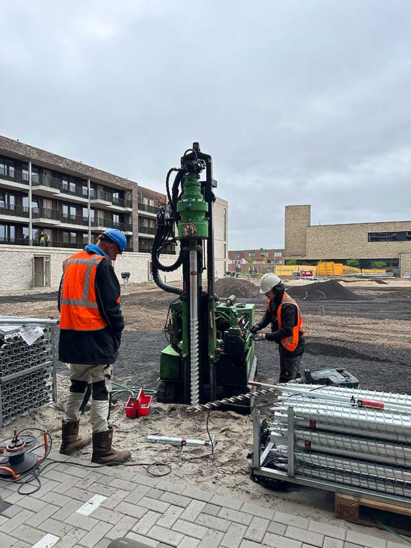Twee Van Aken monteurs plaatsen schroefpaal van 9 meter met groene boormachine op bouwplaats Woerden