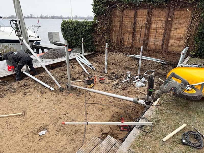 Plaatsing van schroefpalen type V76 voor vlonderfundering aan het IJsselmeer in Almere, met zichtbaar compact hydraulisch materieel en palen in kleigrond